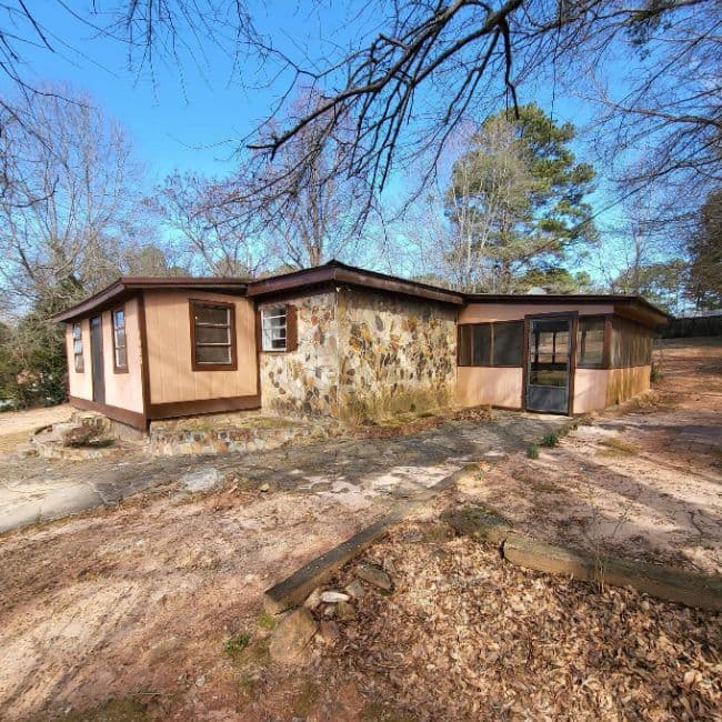 Single-story home with stone and brown siding in a wooded yard.